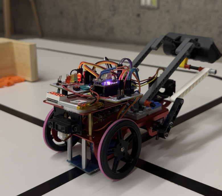 Skidsteer robot with a red chassis, black wheels, breadboard electronics, and a claw arm, on a white track with a black line