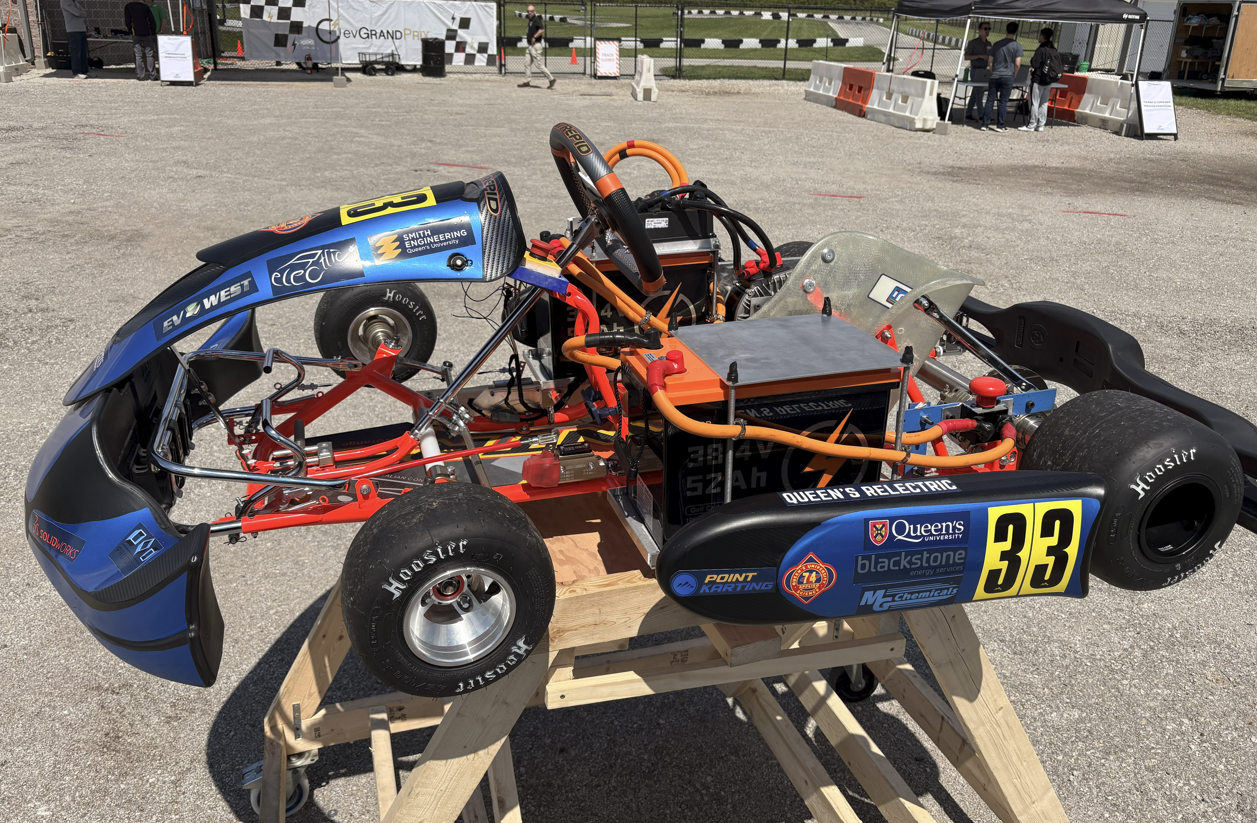 Queen's Relectric electric go-kart, number 33, on a stand at an EV Grand Prix competition with sponsor decals visible