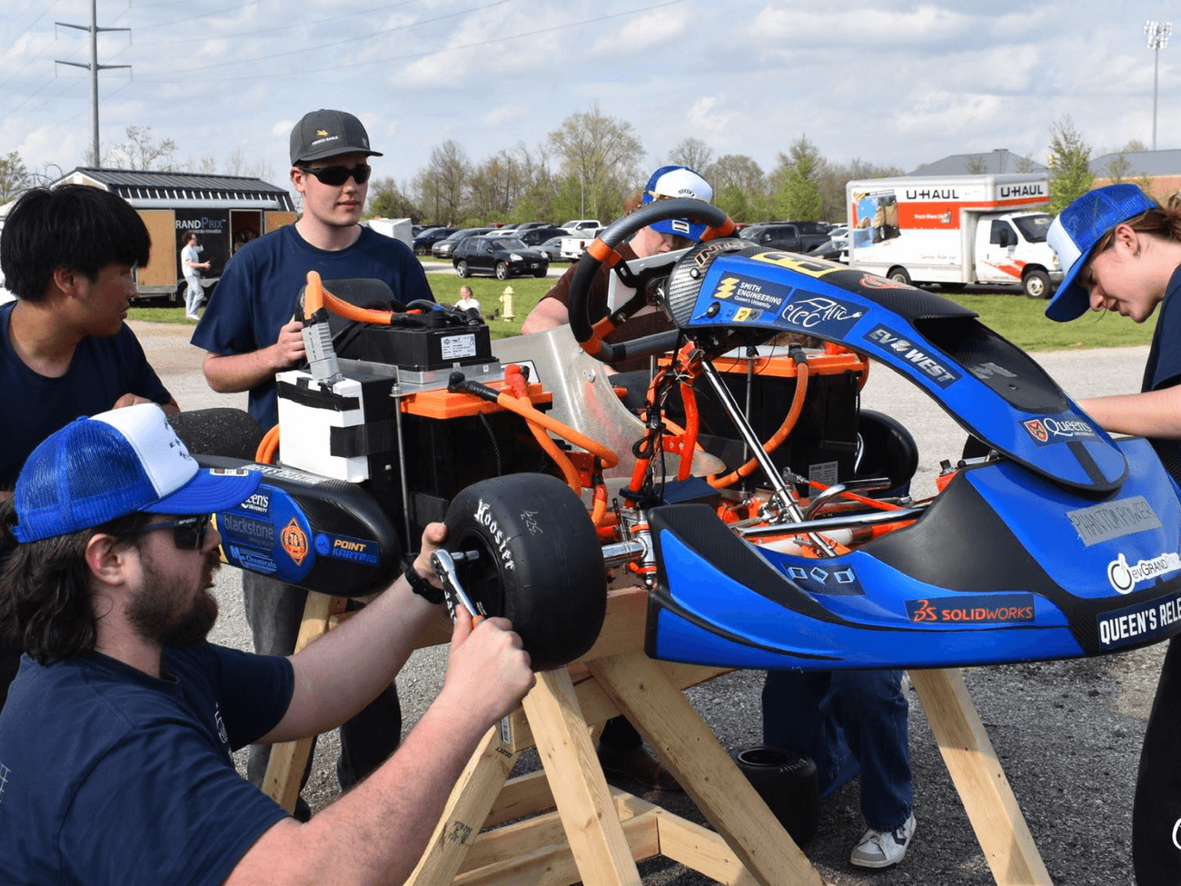 Team members working on the go-kart at the Purdue EV Grand Prix, with the Relectric livery and sponsor decals visible