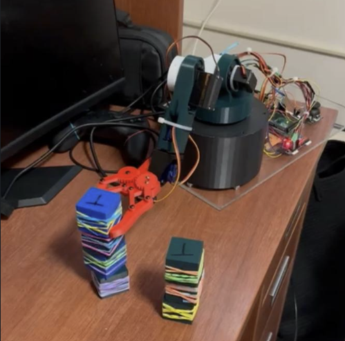 Robotic arm with a red gripper next to two partially built cube stacks on a desk